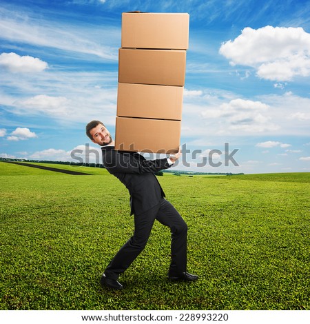 smiley young businessman looking at camera and carrying four heavy boxes on the hands. photo at outdoor