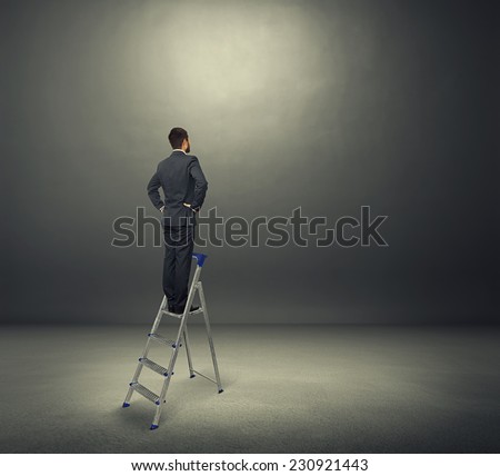 concentrated businessman standing on the stepladder and looking forward. photo in the dark room