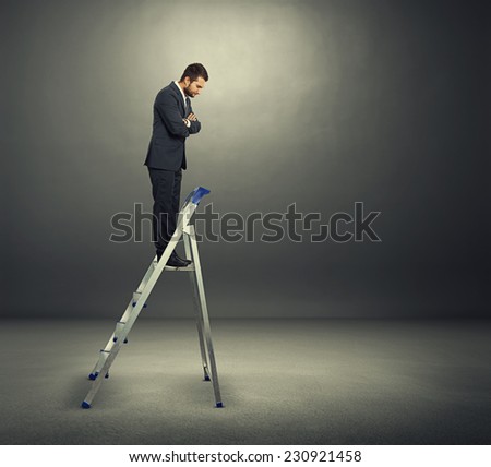 displeased businessman standing on the stepladder and looking down. photo in the dark room