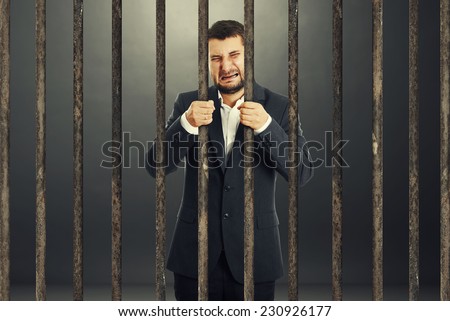 crying businessman behind the prison cell over dark background