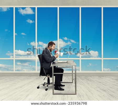angry businessman screaming with megaphone and looking at laptop in the light office with big windows