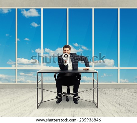 angry businessman screaming with megaphone and looking at camera in the light office with big windows