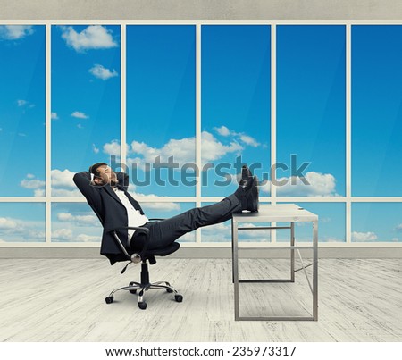 young businessman put his feet up on the table, resting and smiling in the light office with big windows