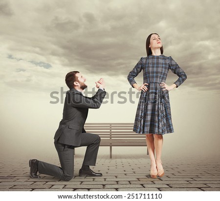 sad man kneeling on one knee, looking at young attractive woman and asking for forgiveness. photo at outdoor