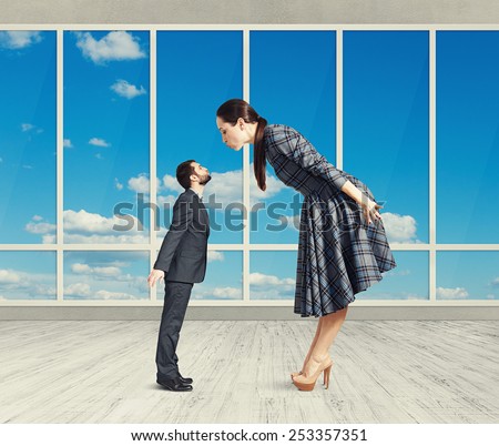 big woman bending forward and kissing small man. photo in room with big windows