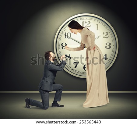 angry yelling woman and crying man in dark room with big clock on the wall