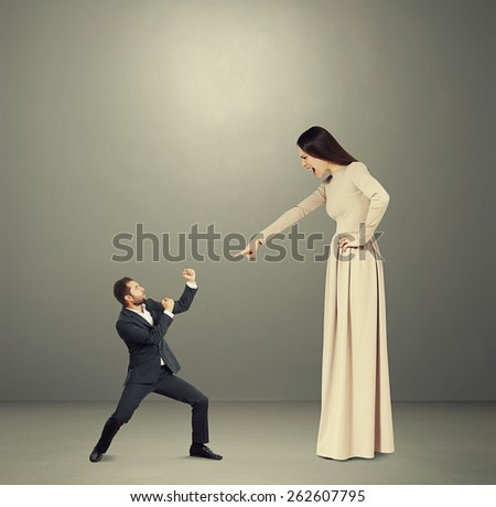 small man waving his fists and looking at angry screaming woman against dark background