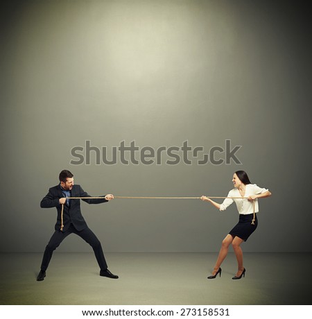 woman and man in formal wear pulling the rope over dark grey background
