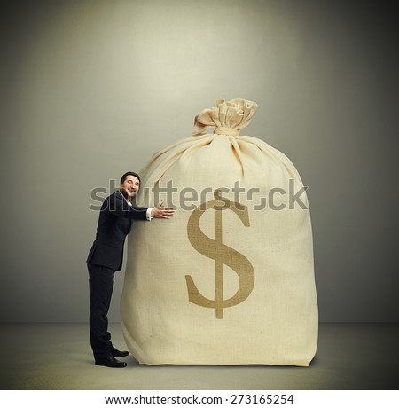 happy man embracing big bag with money over dark grey background