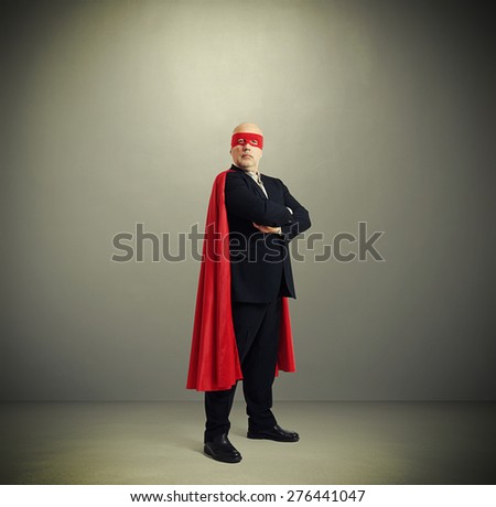 assured senior businessman wearing like super hero in red mask and cloak over light grey background