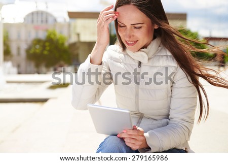urban photo of smiley young woman holding tablet pc and looking at screen