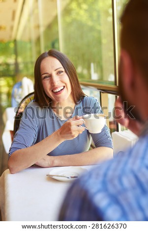 laughing woman holding cup of coffee and looking at man. loving couple on a date at cafe