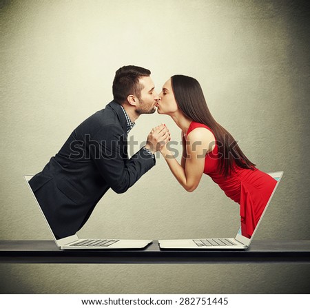 handsome man got out of the computer and kissing beautiful young woman who got out of another computer over dark background