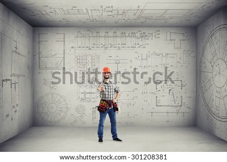 smiley handyman with tools on the belt showing thumbs up and standing in empty room with prints on the walls and ceiling