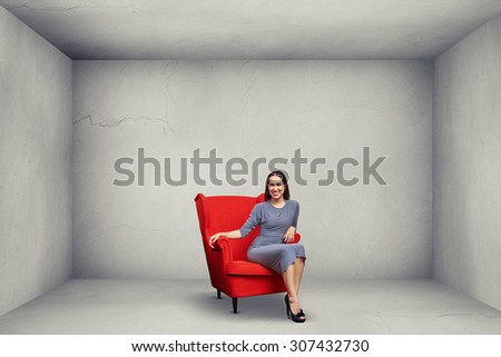 smiley woman sitting on red chair in empty grey room
