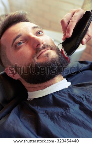 barber shaving beard with electric razor of client in professional barbershop