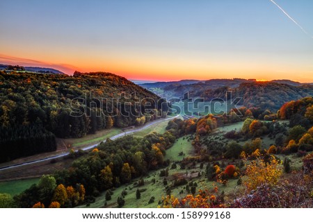 Idyllic Autumn Scenery with Colorful Orange Golden Trees near a lovely Country Road in the rocky Jura Mountains of Bavaria, Germany. Sunset in Fall with a wonderful clear sky in the rural countryside.