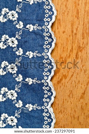 jeans fabric with white flower embroidery laid over plywood background