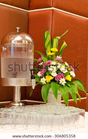 Water dispenser with glasses and flower vase on table at reception table