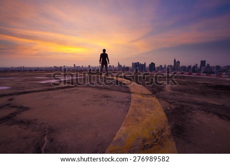 Yellow line lead to a man standing on the concrete floor of a skyscraper rooftop building watch a city sunset