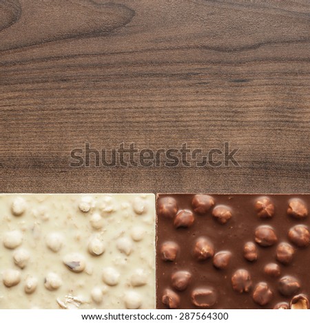 black, milk and white chocolate bars with whole hazelnuts on wooden table