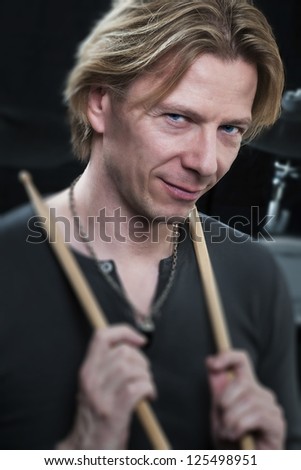 Man in front of a black background an his drums is holding drumsticks and is looking to the viewer