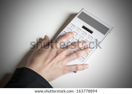 Picture of a female hand typing on a white calculator with empty display