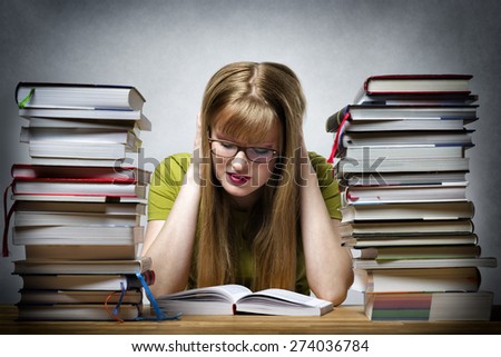 young woman with lots of books at a table is reading bored book