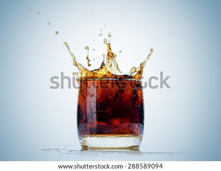 Ice cube droped in cola glass and cola splashing on background