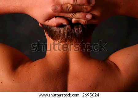 Close up of a male model\'s back, hands behind his head on a black background