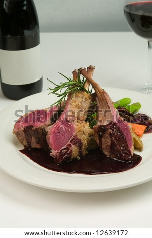 Lamb chops with a glass and bottle of wine on a white table.
