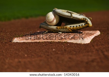 Baseball in a mit sitting on the grass and dirt of a diamond