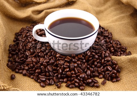 Cup of coffee sitting in a bed of coffee beans on top of a canvas bag
