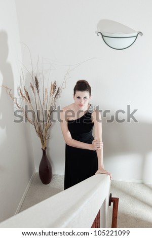 Beautiful young brunette woman standing at the bottom of the stairs, apparently waiting for someone; dramatic lighting