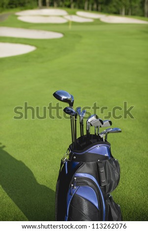 Golf bag and clubs in front of de focused green with sand traps