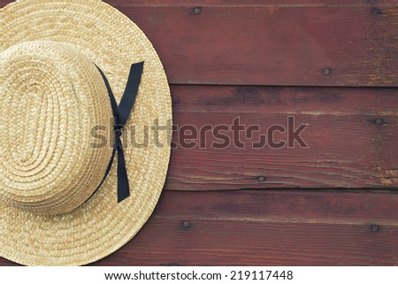 An Amish man\'s straw hat hangs on a red, wooden barn door