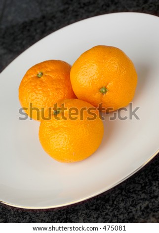 Three satsumas on a white plate, on a grey granite worktop, shot at an angle