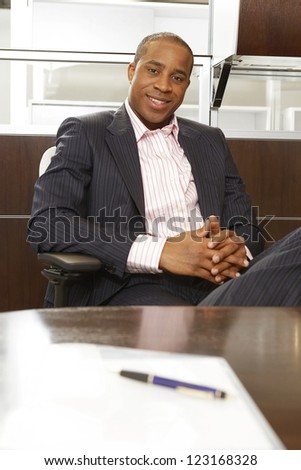 Successful African businessman relaxing in a chair in front of his desk at the office