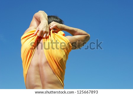 man pulling up his shirt at the back, showing his back with blue sky at the background