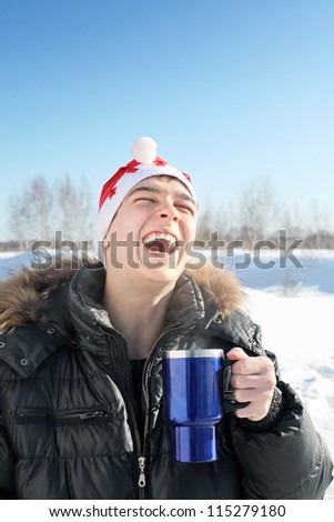 laughing young man in santa\'s hat with travel mug in the winter