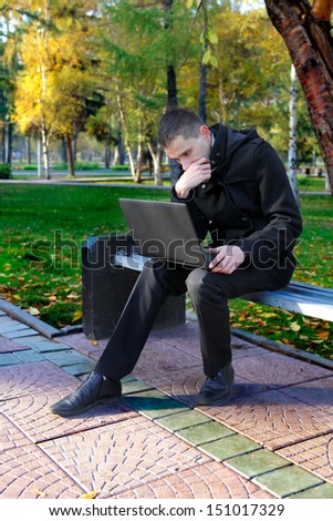 Serious man with Laptop sitting on the bench at the Autumn Park