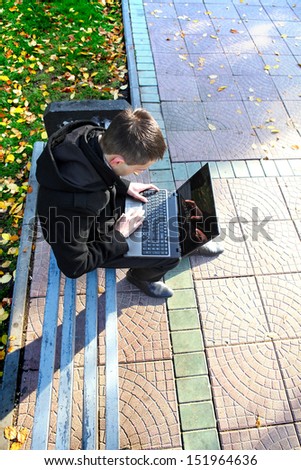 Young man with Laptop sitting on the bench at the Autumn Park