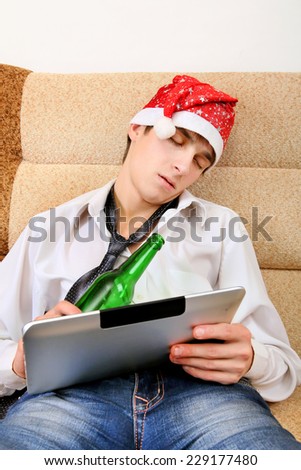 Tired Teenager sleeping in Santa Hat with Tablet Computer and Bottle of the Beer at the Home