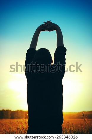 Vignetting Photo of the man silhouette with hand up on sunset background