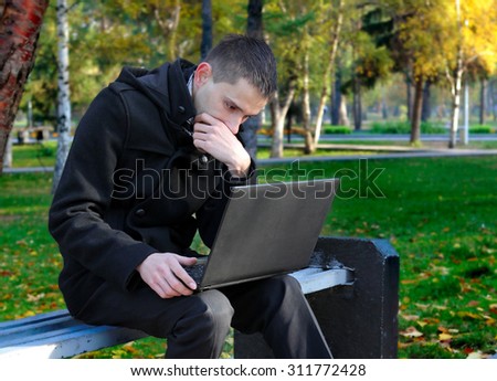 Serious Young Man with Laptop in the Autumn Park