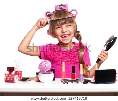 Portrait of pretty little girl seating at table with makeup accessories on white background