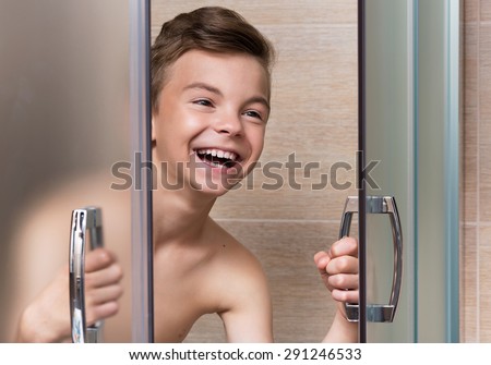Smiling beautiful teen boy takes a shower in the bathroom
