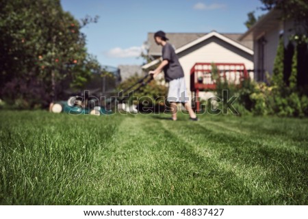 Teenage boy mowing lawn (extremely shallow depth of field, focus in foreground)
