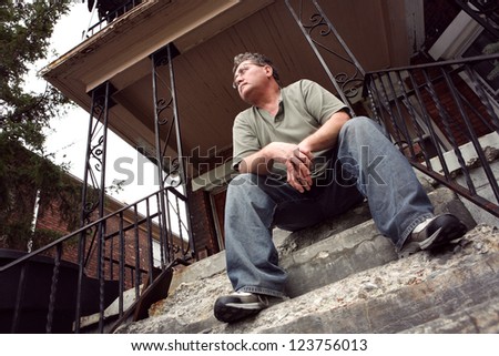 Middle aged man sitting on the steps of a house