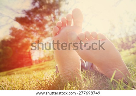 Barefoot child lying on green grass outdoors.  Instagram effect